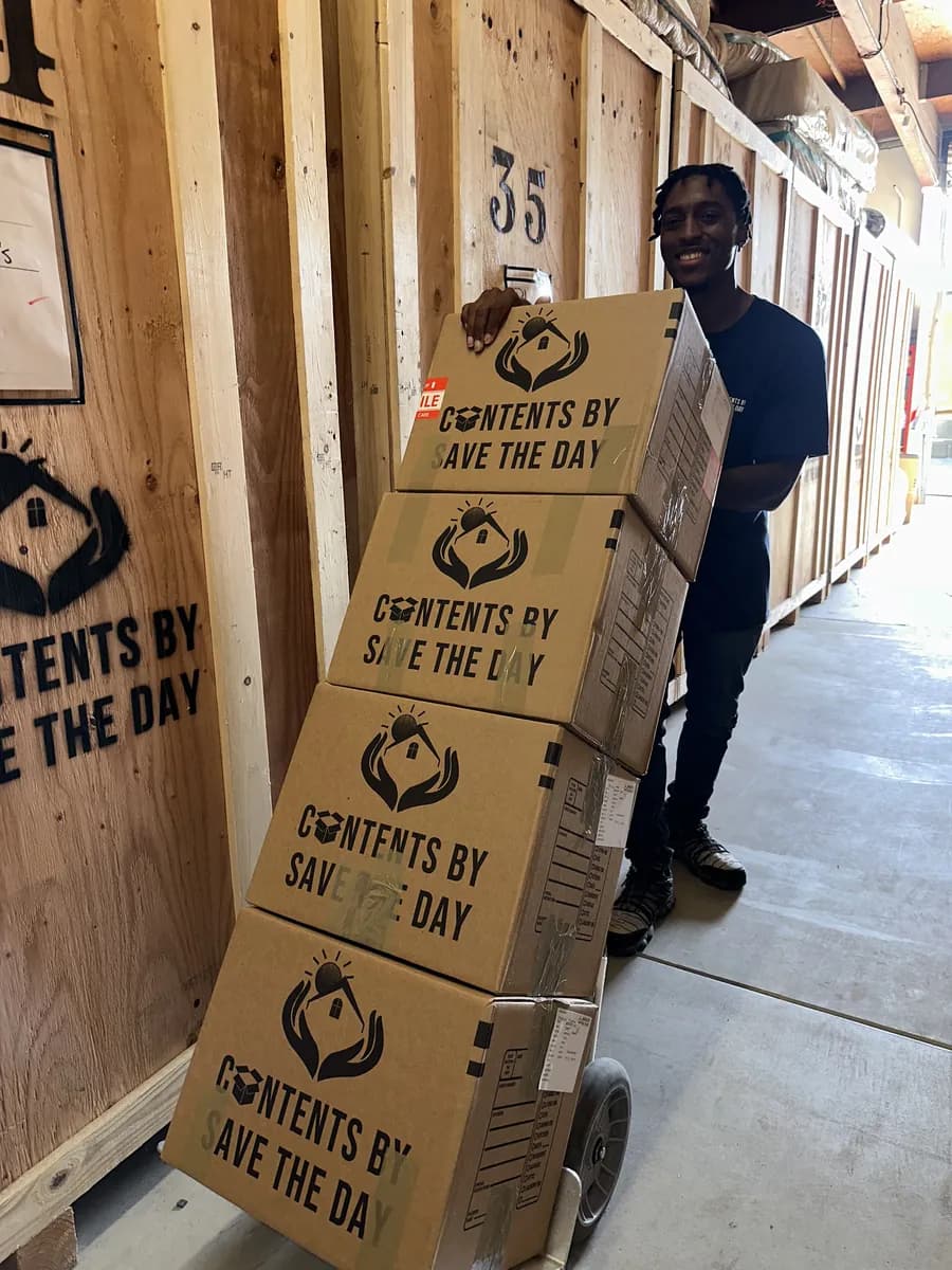 Smiling Contents by Save The Day crew member moving branded boxes on a hand truck through the warehouse