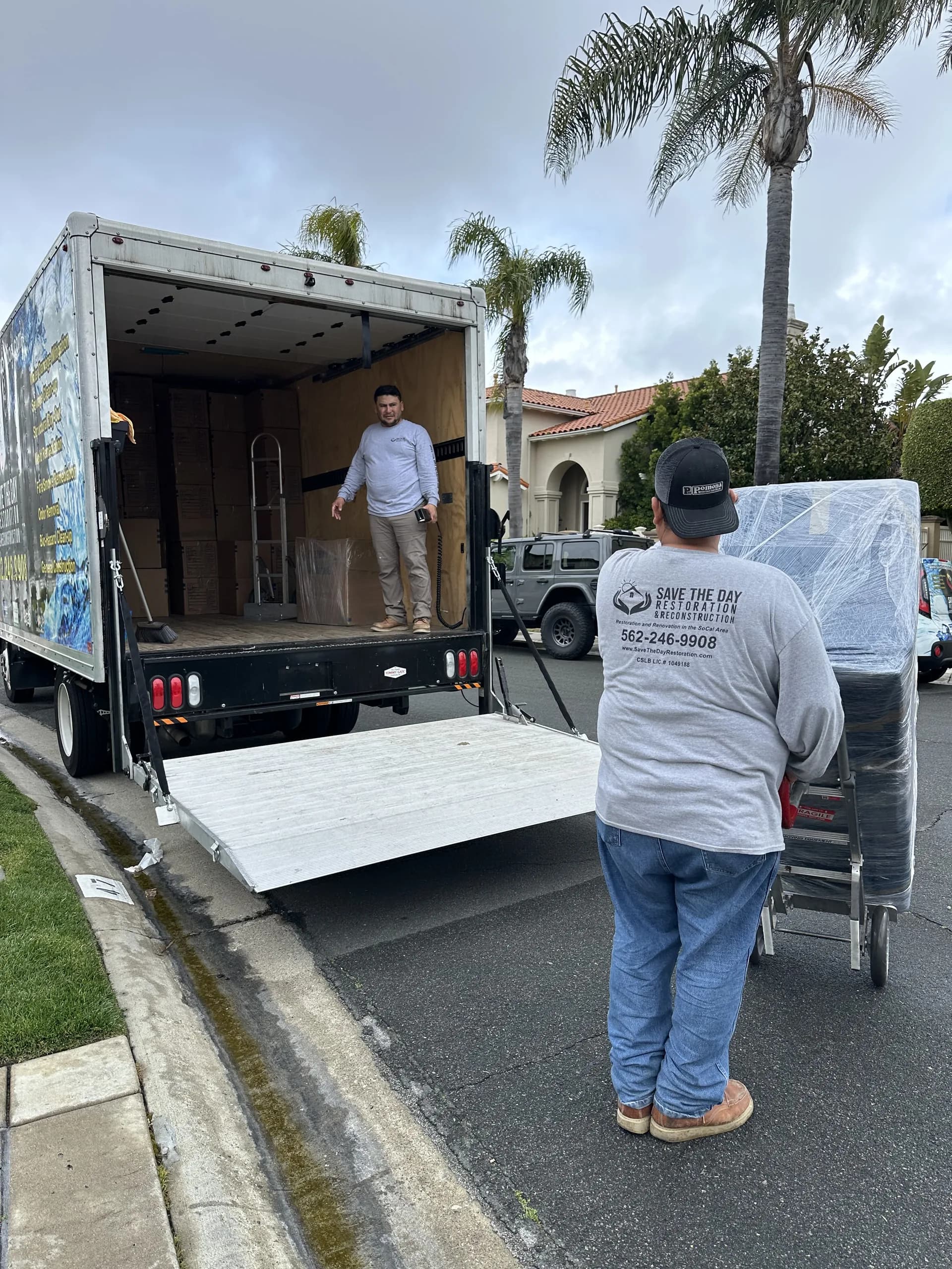 Crew member moving a shrink-wrapped item on a hand truck to a branded box truck during pack-back
